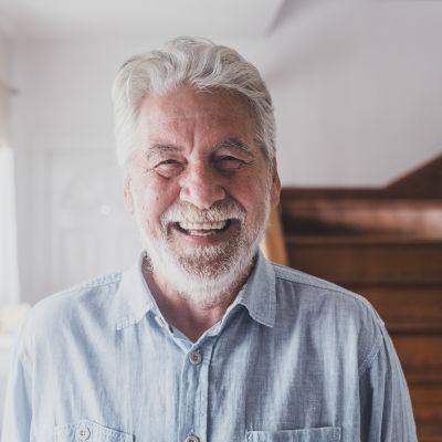 close up portrait of an older man smiling in front of a staircase