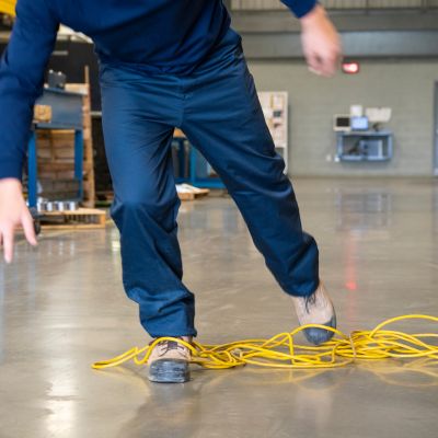 Man tripping over a yellow power cord in a warehouse.