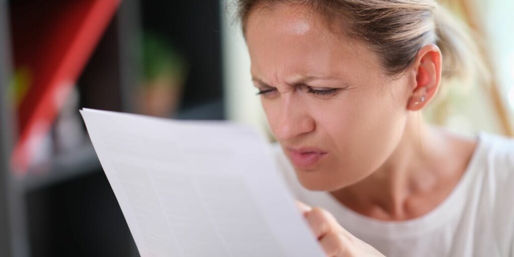 Woman squinting trying to read a page that she's holding close to her face.