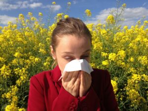 young woman blowing her nose outdoors in front of tall yellow flowers