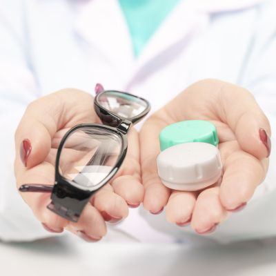 eye doctor holding glasses in one hand and a contacts lens case in the other, helping choose between contacts vs. glasses