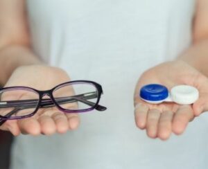 person holding glasses in one hand and a contacts lens case in the other