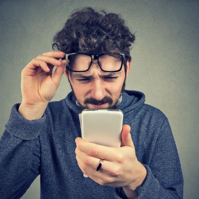 man pulling up glasses while squinting at his smartphone