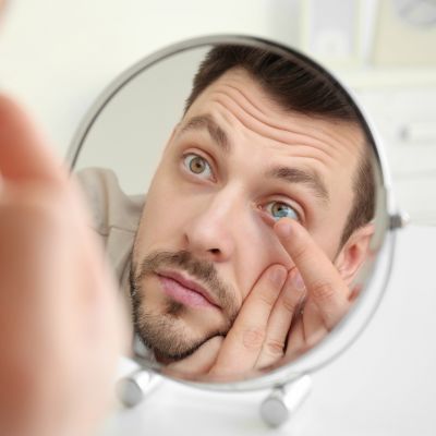 young man putting contact lenses in front of mirror at home