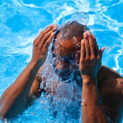 man in swimming pool splashing water in his face