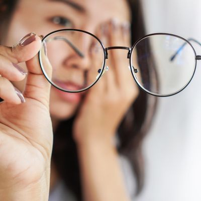 Young Asian woman suffering fry dry eye removing her glasses and rubbing her eye.