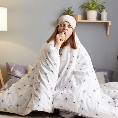 Woman in bed wrapped in her blanket yawning due to lack of sleep.