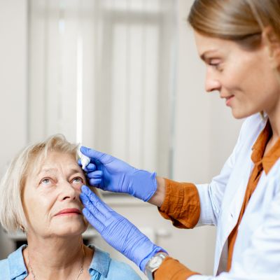 younger female eye doctor helping an older female patient put in eye drops