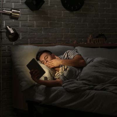 oung man suffering from sleep deprivation with tablet computer in bedroom at night