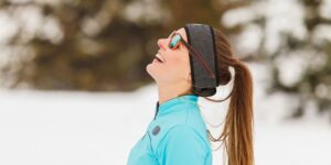 young woman in sunglasses and sports wear outside on a snowy day looking at the sky and smiling